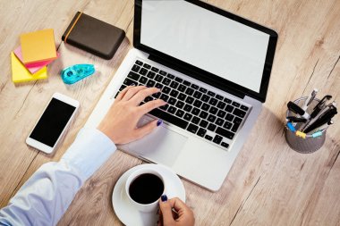 Bir kadın en iyi görünümü çalışma dizüstü ve holding fincan kahve eller. Smartphone ve farklı ofis aksesuarları masaya. 