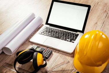 Laptop ve sarı kask ile architectonic bir çalışma alanının üstten görünüm. Farklı aksesuarlar, planları ve kahve masada olduğunu. 
