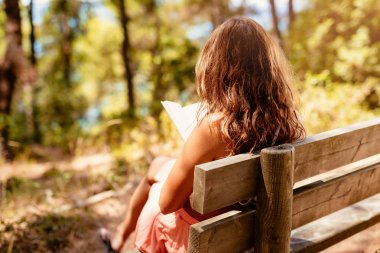 Genç kadın ormanda dinlenirken bir kitap okuma.