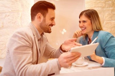 İki güzel genç gülümseyen insanlar kafede oturan ve dijital tablet üzerinde çalışan.