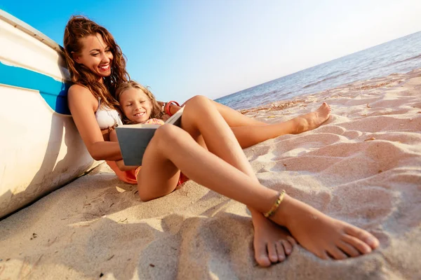 美しい小さな女の子や若い女性砂浜のビーチでの読書 彼女は彼女の顔に笑みを浮かべてボートの横に座ってください — ストック写真