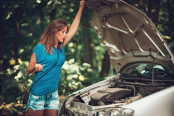 森の道を打破する車と美しい若い女性 彼女はエンジンを見ながら車と持株レンチに地位を持っています — ストック写真