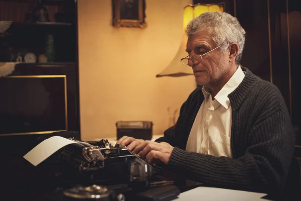 Retro Senior man writer with glasses writing on obsolete typewriter.