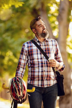 Casual işadamı bisikletle işe yarayacak. Bisiklet ve düşünme yanında kahve ile yürüyor.