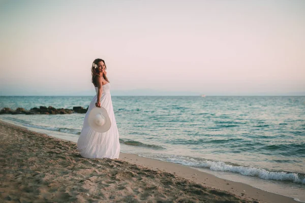 Bela Jovem Mulher Sorridente Vestido Branco Andando Praia Segurando Chapéu — Fotografia de Stock