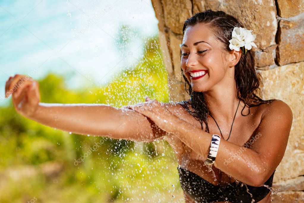 Beautiful young woman enjoying under a shower on the beach. 