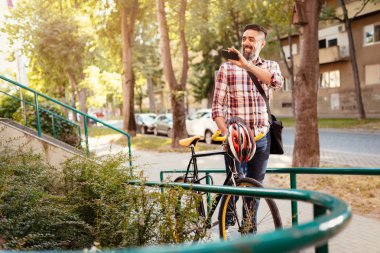 Casual işadamı bisikletle işe yarayacak. O bisiklet yanındaki yürüme, smartphone holding ve Merhaba sallayarak.