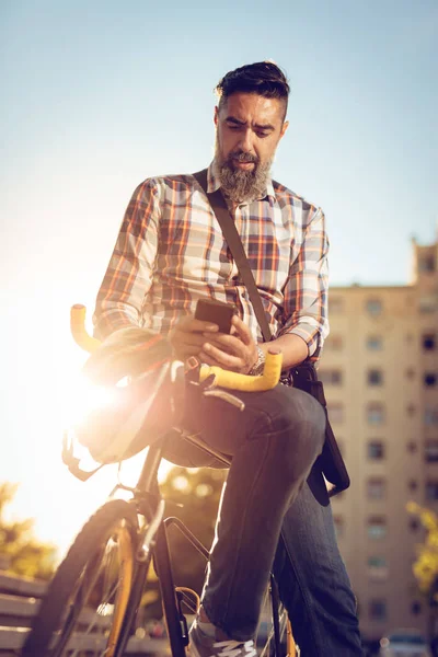 カジュアルなビジネスマンは自転車で仕事に行きます 彼は自転車の上に座っては テキスト メッセージを送信します — ストック写真