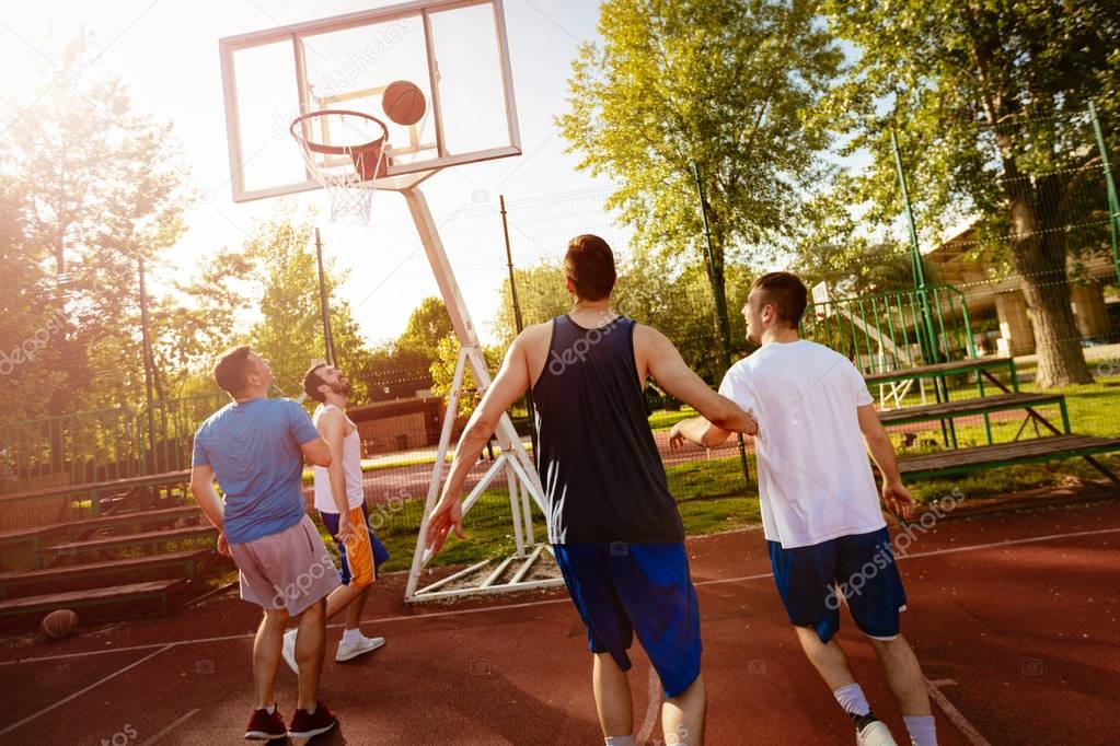 Four basketball players have a training outdoor. They are playing and making action together.