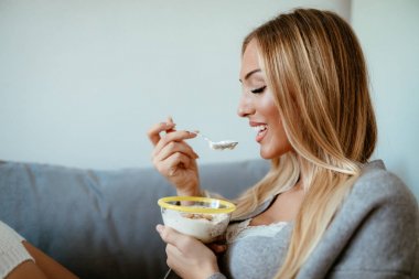Kanepede onun evde yoğurt ile tahıl yemek ve gülümseyen genç kadın.