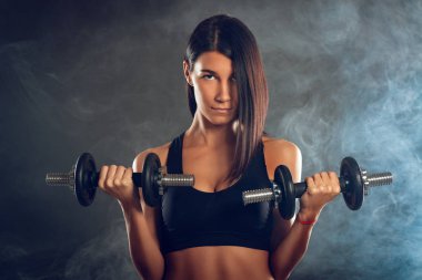 Çekici kas genç kadın koyu arka plan üzerinde dumbbells ile egzersiz yaparak.