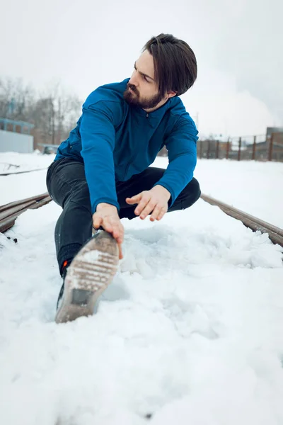 Active young man stretching on old railroad during winter training outside.