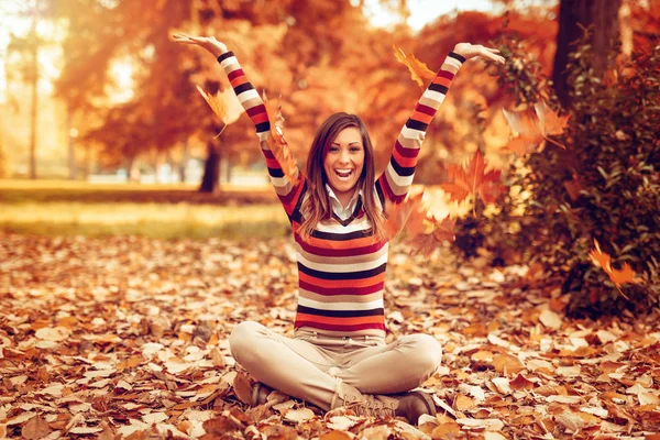 young woman sitting on ground covered with leaves and having fun