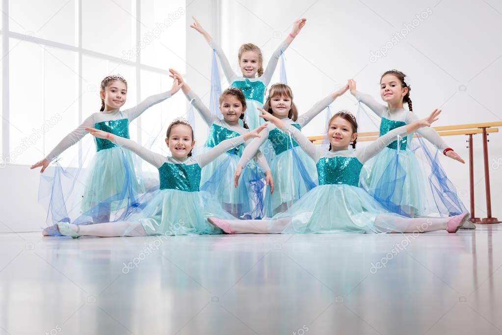 Smiling little girls in dresses practicing postures during ballet class. Looking at camera.