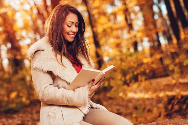 秋の色に日当たりの良い森林の美しいの若い笑顔女性の読書の本 — ストック写真