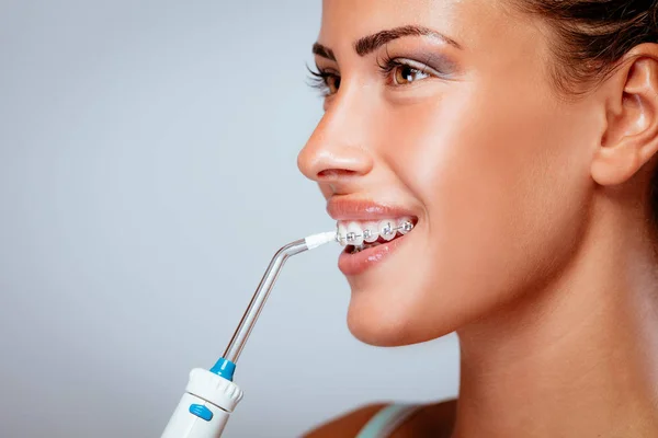 Oral irrigator ile dişlerini Temizleme diş telleri ile gülümseyen genç kadın.