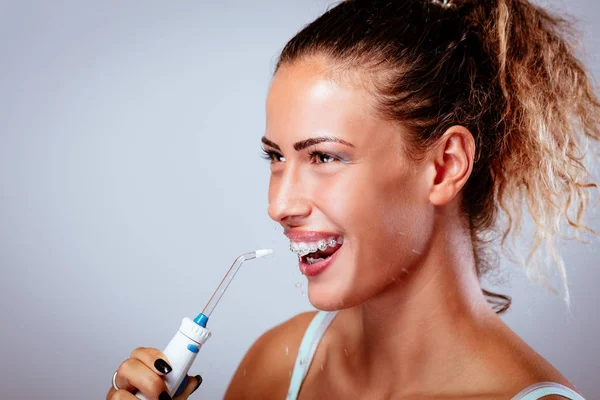 Oral irrigator ile dişlerini Temizleme diş telleri ile gülümseyen genç kadın.