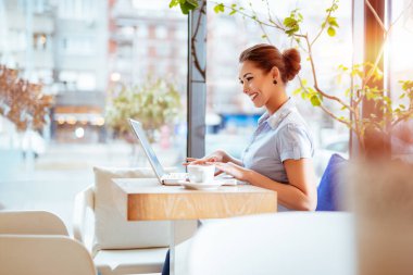 Cafe 'de dizüstü bilgisayarda çalışan genç bir kadın.