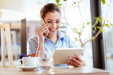 Smartphone kullanarak ve dijital tablet üzerinde çalışan genç iş kadını