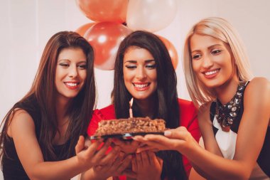 Üç gülümseyen kadın doğum günü pastası ellerine bakarak