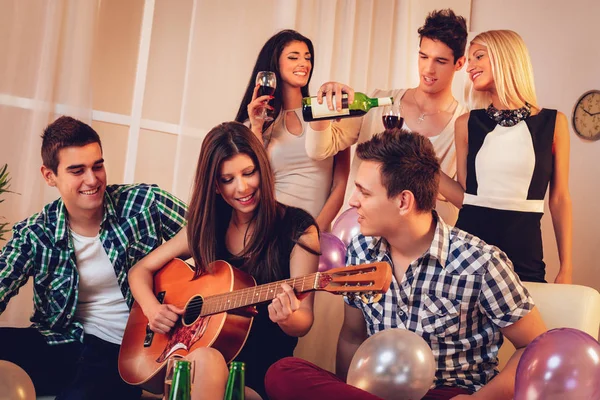 Young woman playing on guitar to friends at party