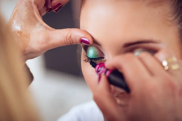 Makeup artist applying the mascara to model