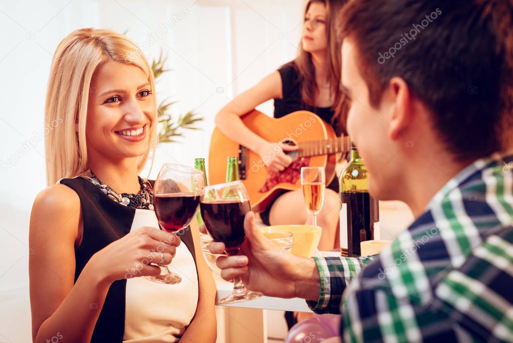 Young woman and boyfriend toasting with red wine at house party