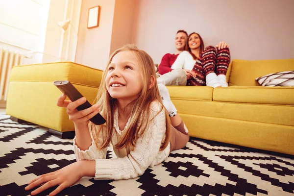 Young Family Watching Girl Lying Floor Holding Remote — Stock Photo, Image