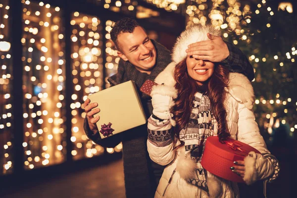 Young man giving gift to girlfriend in city street at Christmas time