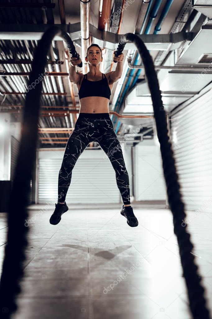 Young muscular woman exercising with ropes at garage gym