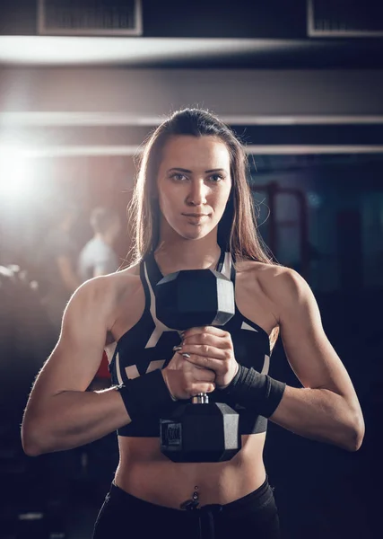 Young muscular woman holding heavy dumbbell in front herself
