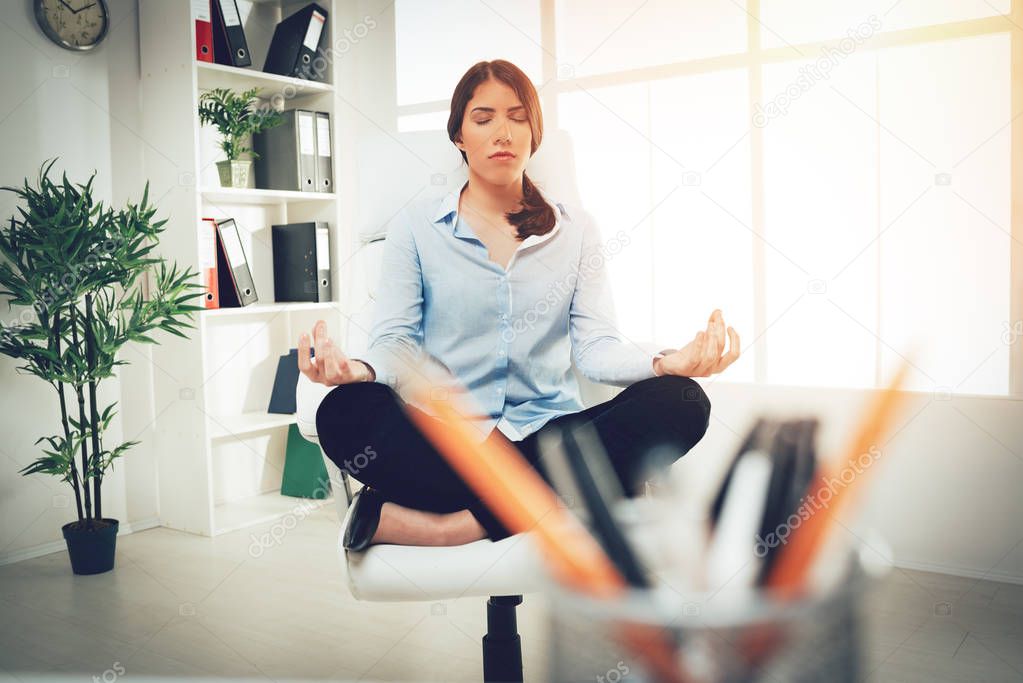 young businesswoman sitting in lotus pose and meditating in office