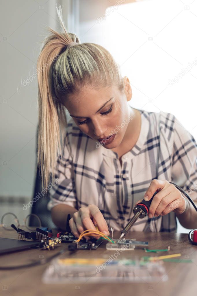 Young woman technician focused on repairing of electronic equipment by soldering iron