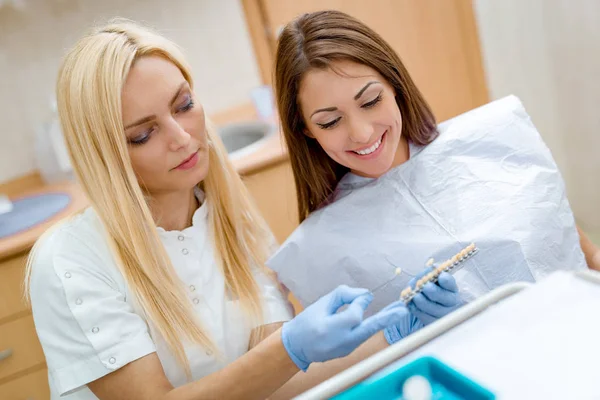 若い女性は笑みを浮かべて訪問歯科医のオフィスと磁器の王冠を示す女性歯科医 — ストック写真