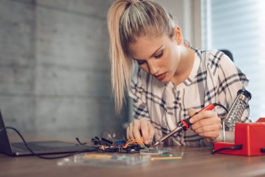 Genç kadın teknisyeni havya tarafından elektronik donatımın tamiri üzerinde duruldu