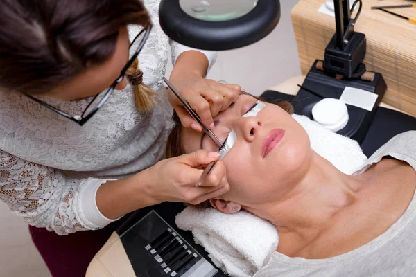 Beautician applying extended eyelashes to young woman in beauty-salon