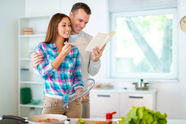 美丽的年轻夫妇在家庭厨房里煮健康的饭菜 他们正在阅读食谱从食谱 — 图库照片