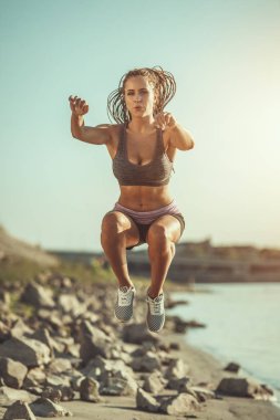 Genç bayan nehir kenarında egzersiz yapıyor. Zıplıyor ve sabah antrenmanı yapıyor..