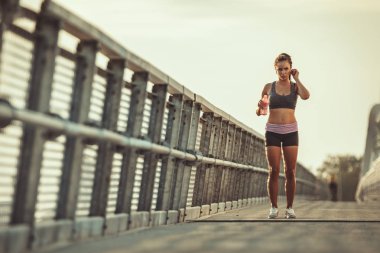 Genç bayan koşucu su içiyor, koşmaya hazırlanıyor ve bir nehir köprüsünde sabah antrenmanı yapıyor..