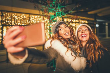 Neşeli genç kız kardeşler gecenin bir yarısı şehir caddesinde eğleniyor ve komik selfie çekiyorlar.. 