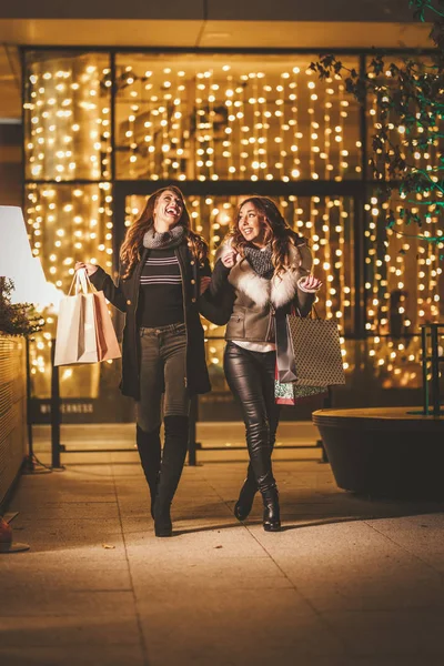 二人の姉妹はショッピングで夜を楽しみ 彼らの手にショッピングバッグで笑って — ストック写真