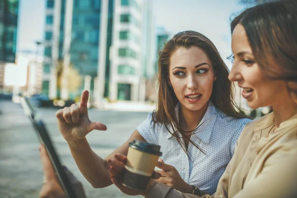 Business women are sitting at office park while using digital tablet and holding disposable coffee cup. Business team is working online together while consulting.