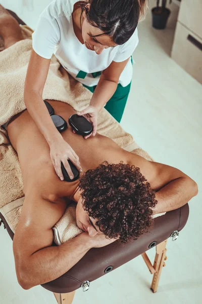 Joven Guapo Disfrutando Durante Masaje Espalda Con Piedras Calientes Spa —  Fotos de Stock