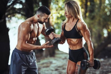 Çekici kaslı kadın vücut geliştirici, nehir kenarındaki doğada kişisel antrenörle sıkı egzersizler yapıyor.. 