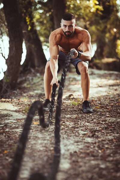 筋肉質の若い男が自然の中でロープで演習をしているフィット — ストック写真