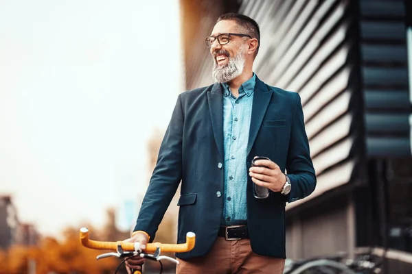 コーヒーを飲みながら自転車でオフィス街の前を歩くことに成功したハンサムな中年ビジネスマン — ストック写真