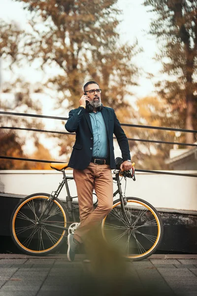A handsome middle-aged man goes to work by bicycle and talking on the smartphone.