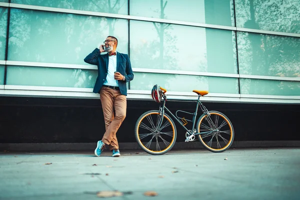 自転車の横に立ってオフィス街の前でスマートフォンを使っています — ストック写真