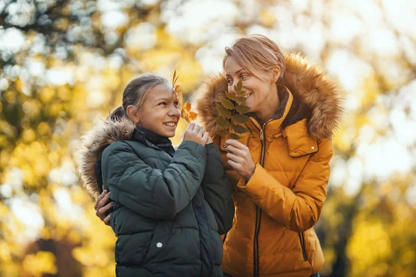 美丽的母亲和她快乐的十几岁的女儿在公园里抱着秋天的树叶 微笑着 — 图库照片