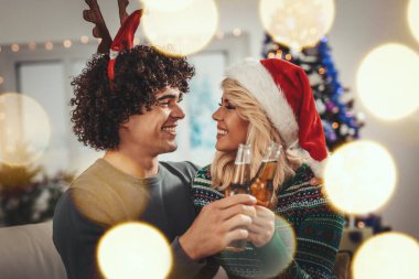 Sıcak, sıcak kazaklar giyen sevgili çift Noel 'de oturma odasında vakit geçirir. Gülümser, eğlenir ve birayla eğlenir..